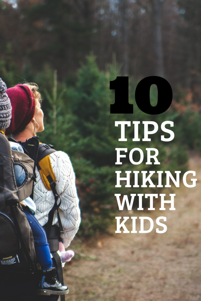 A woman with a red hat hiking on a trail with a child in a woolen hat in a hiking carrier used as an image for 10 Tips for Hiking with Kids.